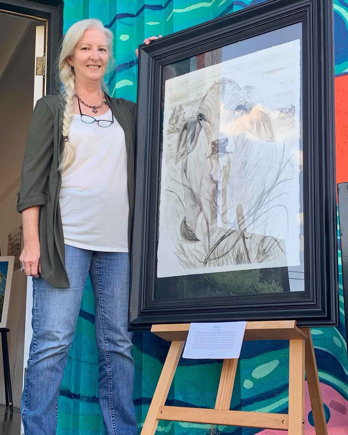 The framed painting of Whisper, with Madison Woods (the artist) for size context.